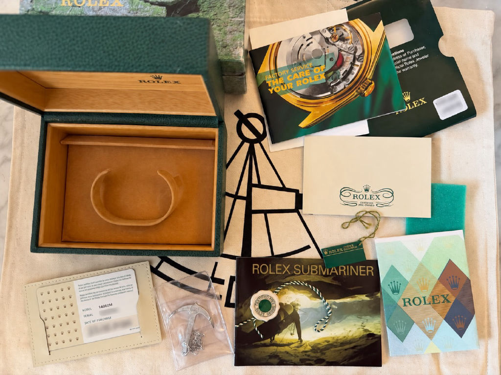 A Submariner box, warranty card, service booklet, anchor and swing tags laid out on linen